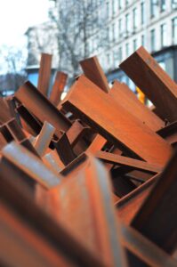 A visually striking close-up of stacked rusty iron beams in an urban setting, reflecting industrial decay.